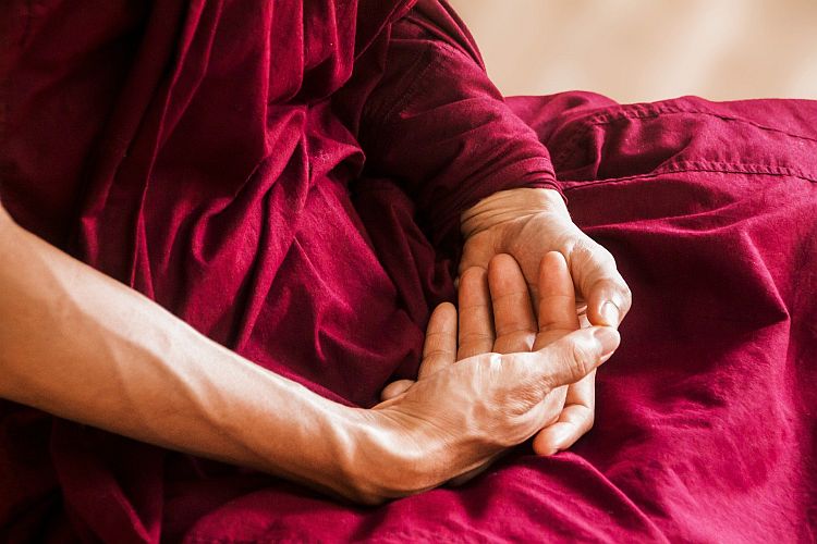 Image of meditating Buddhist monk in red robes sitting with hands in lap